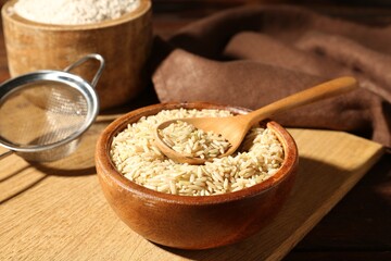 Brown rice, flour and sieve on wooden table, closeup