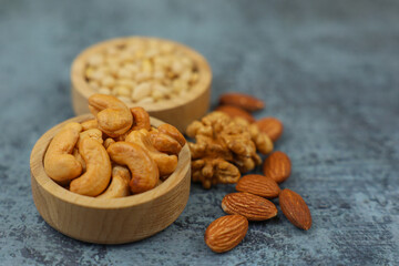Close-up view from above of wooden cashew bowls and pine nut bowls out of focus, which stand on the side surrounded by walnuts and almonds on a gray background with space for text. The concept of