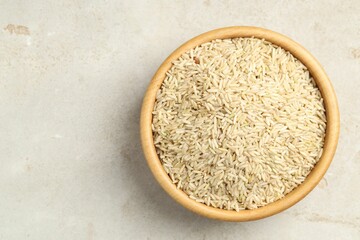 Brown rice in bowl on light grey table, top view. Space for text