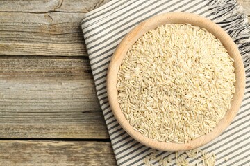 Brown rice in bowl on wooden table, top view. Space for text