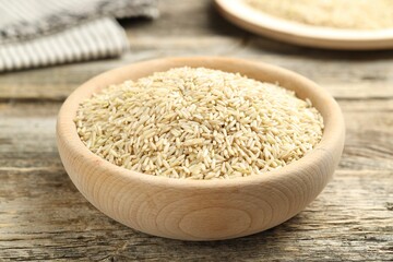 Brown rice in bowl on wooden table, closeup