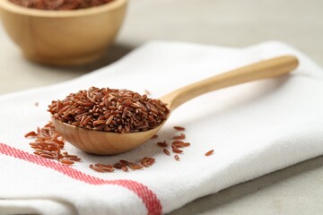 Brown rice in wooden spoon on light grey table, closeup