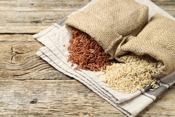 Different types of brown rice in sacks on wooden table, closeup. Space for text