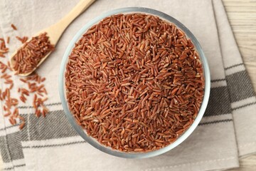 Brown rice in glass bowl and spoon on wooden table, flat lay
