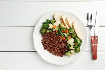 Tasty brown rice with vegetables and chicken on white wooden table, flat lay. Space for text