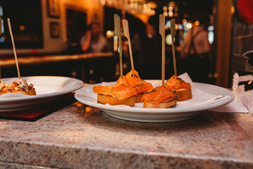 Delicious salmon tapas served on a white plate in a moody bar setting.