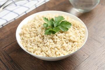 Delicious brown rice with parsley served on wooden table, closeup