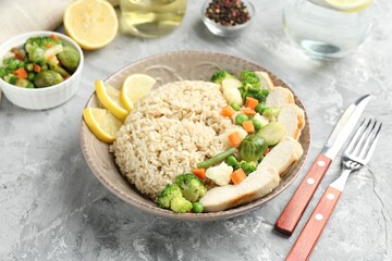 Delicious brown rice with chicken, vegetables and lemon slices served on grey textured table, closeup