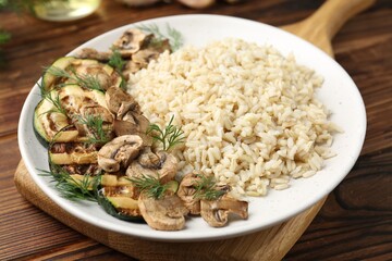Delicious brown rice with mushrooms and dill served on wooden table, closeup