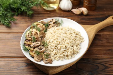 Delicious brown rice with mushrooms and dill served on wooden table