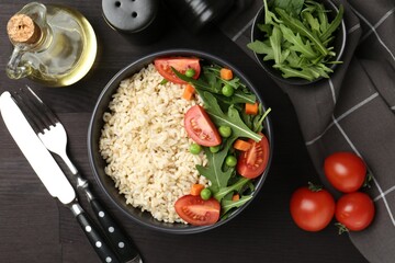 Delicious brown rice with vegetables served on black wooden table, flat lay