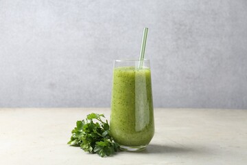 Healthy parsley smoothie in glass and leaves on light textured table against grey background