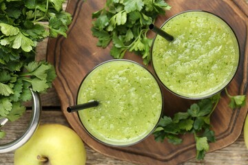 Healthy parsley smoothie in glasses, leaves and apple on wooden table, flat lay