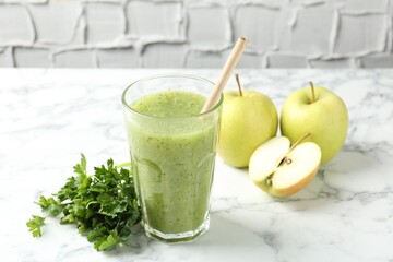 Healthy parsley smoothie in glass, leaves and apples on white marble table against grey textured...
