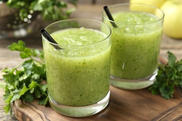 Healthy parsley smoothie in glasses and leaves on wooden table, closeup