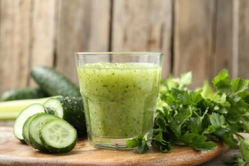 Healthy parsley smoothie in glass, leaves and cucumber on wooden table, closeup