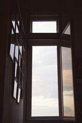 Soft light fills the room as an open window reveals a cloudy sky. Framed memories adorn the walls, creating a warm, inviting atmosphere during the evening