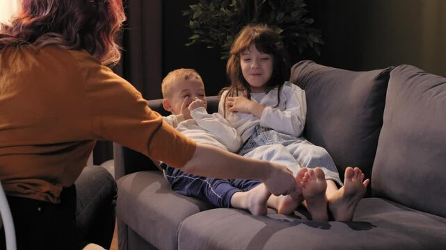 Mother tickling daughter and son on sofa