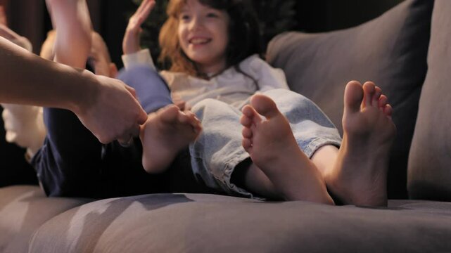 Mom tickles feet of two laughing children lying on sofa