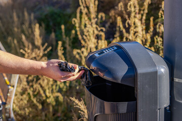 Dog owner throwing poop bag in a public trash can promoting responsible pet ownership