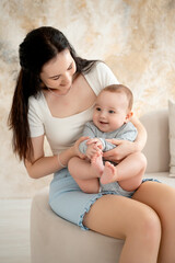 mom and baby, mother hugs and kisses baby holding him in her arms, maternal love and care, young mom having fun with baby baby, mom's decree