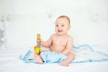 A baby boy plays with a rattle at home on the bed, a small child plays with a bright toy, early...