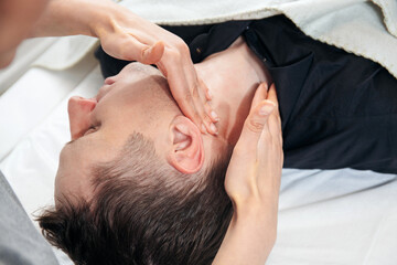 A massage therapist gives a facial and neck massage in a massage parlor