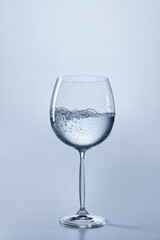 Photo of clear stemmed glass with transparent water, showing subtle bubbles, against soft blue background. Sparkling water. Mock up. Concept of refreshment. Negative space for text, branding