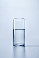 Close-up photo of clear, cylindrical glass filled with transparent water, against soft blue background. Mock up. Concept of hydration, and purity. Negative space for text or branding.