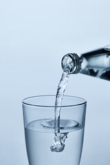 Close-up photo of water being poured from glass bottle into clear glass, showing bubbles and flowing stream against light blue background. Mock up. Concept of nutrition and hydration, drink
