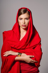 Elegant young woman draped in a vibrant red shawl exudes confidence and style indoors