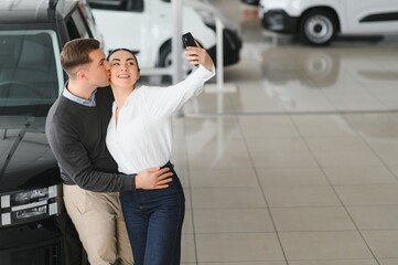 Beautiful young couple at car showroom exited because of buying a new car
