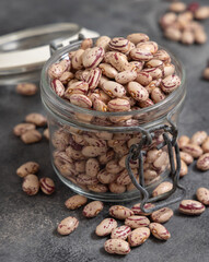 Glass jar full of dried pinto beans on gray closeup. Traditional Latin American legumes