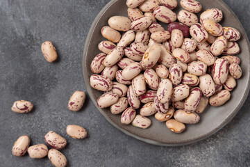 Plate full of dried pinto beans on gray top view, copy space. Traditional Latin American legumes