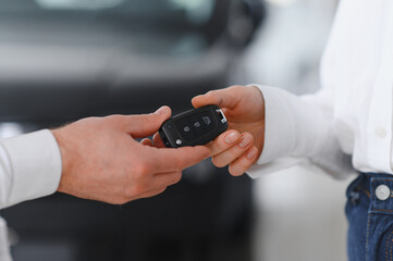 Young Caucasian woman buys a car at a dealership. Bearded man seller gives the car keys