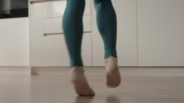 Close-up of a woman dancing at home in casual leggings and socks. The scene captures a joyful and relaxed atmosphere.