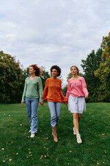 Obraz premium Three stylish women walk hand in hand through a lush green park, exuding confidence and charm