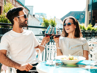 Smiling beautiful woman and her handsome boyfriend. Happy cheerful family. Couple cheering with glasses of red wine at their date in restaurant. They drinking alcohol at veranda cafe in the street