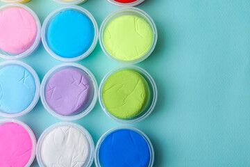 Different colorful modeling clay in plastic jars on light blue background, flat lay. Space for text