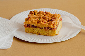 Bright sunlight shines on a piece of sweet homemade pie with jam and crumbs, sitting on a white plate with a fork and napkins. A delicious and calorie-rich treat prepared from a simple recipe.