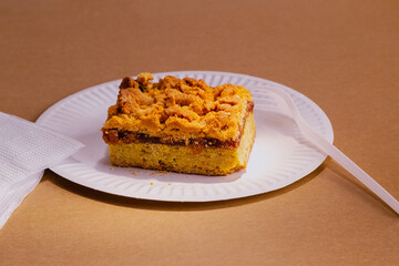 Bright sunlight shines on a piece of sweet homemade pie with jam and crumbs, sitting on a white plate with a fork and napkins. A delicious and calorie-rich treat prepared from a simple recipe.