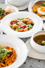 A beautifully arranged table featuring a variety of dishes, including a salad with vegetables and seafood, pasta, curry, and sides, all beautifully presented in white dishes.