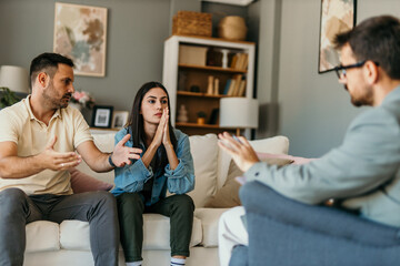 Young couple arguing during therapy session with psychologist