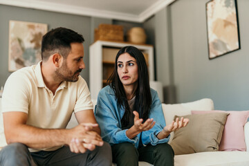 Worried couple arguing and discussing problems sitting on sofa at home