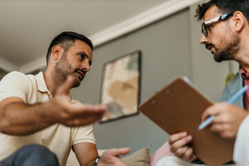 Patient explaining his problems to psychologist taking notes during therapy session