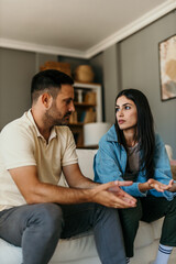Young couple arguing and gesturing while sitting on sofa at home