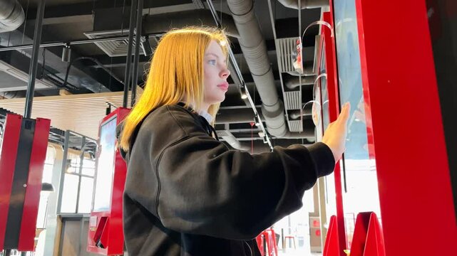 A young woman orders food on a self-service board in a fast food restaurant
