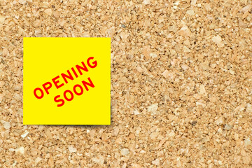 Yellow note paper with word opening soon on cork board background with copy space