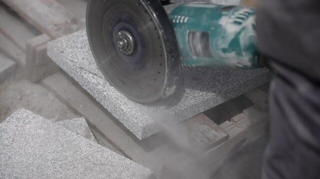 Worker cutting concrete tiles with a grinder tool at a construction site, slow motion