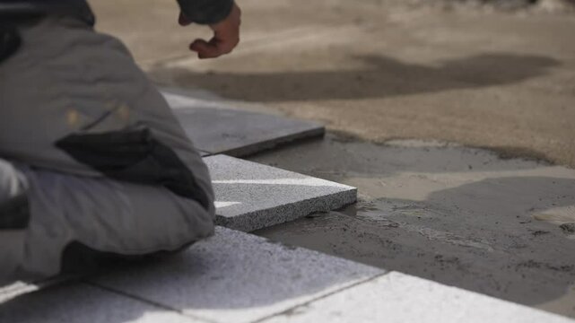 Worker laying pavement stones on a concrete walkway, slow motion